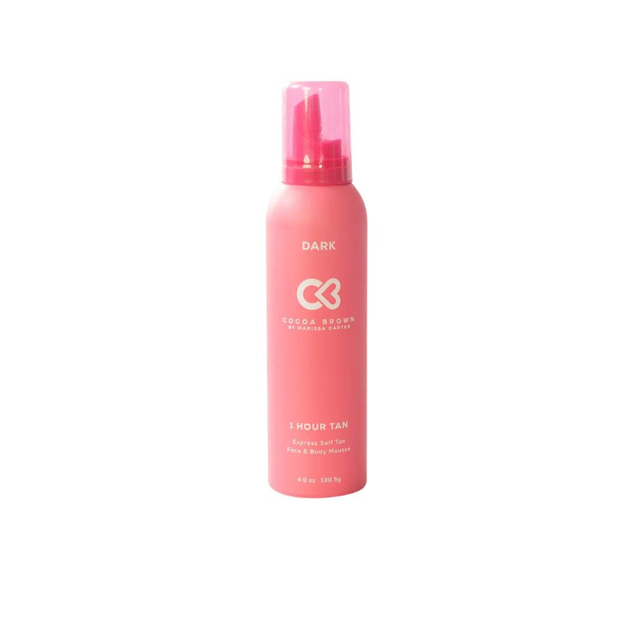 A pink aerosol can of Cocoa Brown 1 Hour Tan hair and body spray, labeled 'DARK', on a solid white background.